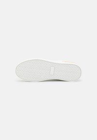 Baskets blanches avec une semelle en caoutchouc texturée présentant un motif en zigzag. Design minimaliste avec un accent doré sur le côté pour le détail.