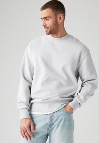 Gray sweatshirt made of cotton blend, featuring a crew neckline and ribbed cuffs. Small branding on chest, paired with light blue jeans.