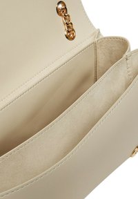 Interno di una borsa a tracolla in pelle beige con texture morbida, accessori in oro, due scomparti e senza motivi o accentuazioni visibili.
