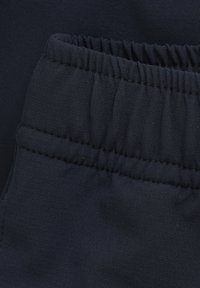 Navy stof met een gladde textuur, voorzien van een elastische tailleband en gestikte zakdetails. Het materiaal is lichtgewicht en zacht.