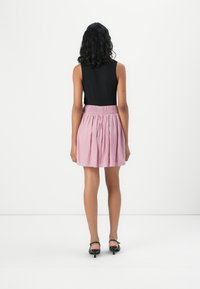 Schwarzes ärmelloses Top kombiniert mit einem rosa gerafften Rock, der einen elastischen Bund, eine glatte Textur und eine ausladende Silhouette aufweist.