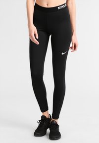 Svarta träningsleggings med en åtsittande passform, elastisk midja med "NIKE"-logotyp och en vit Nike-swoosh på vänster lår.