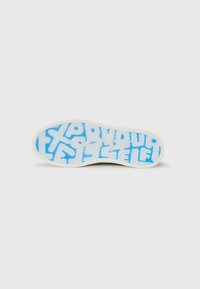 La semelle de la chaussure présente un motif texturé bleu avec une typographie audacieuse sur fond blanc. Sa forme est plate avec un bord arrondi.
