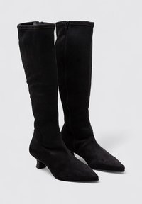 Botas negras de ante hasta la rodilla, con puntera puntiaguda y un bajo tacón cuadrado, y cremallera lateral para ponerlas fácilmente.