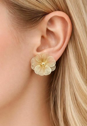 Goldener, blumenförmiger Ohrring mit detaillierten Blütenblättern, getragen am Ohrläppchen einer Person mit heller Haut und blondem Haar.