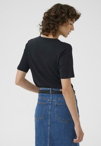 Haut noir à manches courtes, associé à une jupe en denim bleu avec une taille ajustée et deux poches arrière. La tenue a une silhouette moderne et épurée.