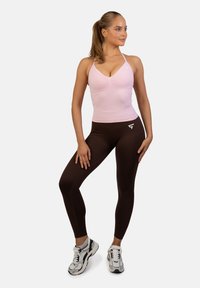 Jasnoróżowy, dopasowany top na ramiączkach z dekoltem w kształcie litery V oraz brązowe legginsy z wysokim stanem. Wykończony białym logo. Charakteryzuje się gładką teksturą i elastycznym materiałem.