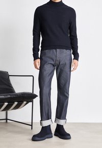 Mörkblå ulltröja med hög krage, mörkblå denimjeans med uppvikta ben, mörkblå mocka ankelstövlar, minimalistisk design, släta texturer.