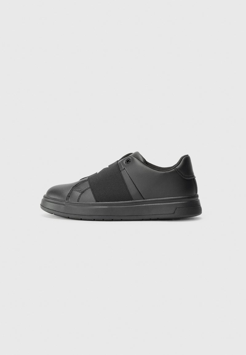 Baskets noires avec une tige en cuir lisse, détail de bande élastique au milieu du pied et semelle en caoutchouc plate. Design minimaliste sans marque visible.