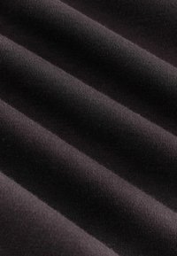 Nahaufnahme von weichem, dunklem Stoff mit sichtbarer Stricktextur und sanften Falten, die diagonale Schatten und Lichtreflexe erzeugen.