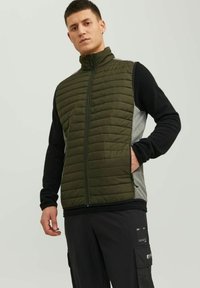 Olivenfarbene Steppweste mit vertikalem Steppdesign, Reißverschluss und schwarzen langen Ärmeln. Verfügt über seitliche Taschen und ein graues Panel an den Seiten.