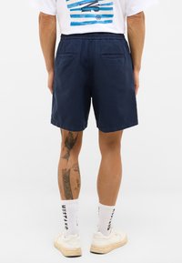 Pantalones cortos de color marino con cinturilla elástica, dos bolsillos traseros y corte recto. La prenda está hecha de una tela ligera.