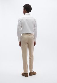 Camisa blanca de manga larga, pantalones beige, zapatos marrones. Material de algodón suave, corte entallado. Dos bolsillos traseros en los pantalones.