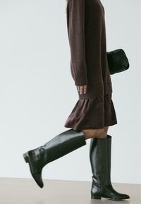 Czarne kozaki za kolano ze skóry o gładkim wykończeniu, noszone z ciemnobrązowym swetrem i spódnicą z falbanami, odpowiednie do codziennego noszenia.