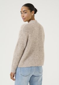 Lichtbruine gebreide trui met een zachte textuur, voorzien van een ribbelontwerp en een ronde halslijn. Draagt een combinatie met lichtblauwe jeans.