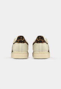 Pair of cream sneakers with leopard print detail on the heel, viewed from the back against a white background.