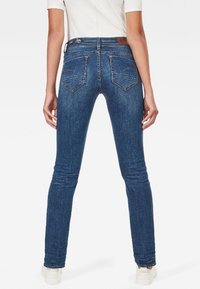 Jeans in denim blu a vestibilità slim con dettagli cuciti, tasche posteriori e una etichetta in pelle sulla vita. Tessuto liscio e finitura leggermente sbiadita.