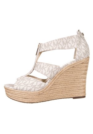 Sandał na koturnie wykonany z jasnobeżowej tkaniny z subtelnym wzorem MK, z plecionym obcasem z juty i paskiem z przodu.