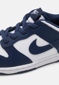 Tengerészkék és fehér sneaker, bőr és hálós anyagokból készült. Különleges jellemzője a fűző, a kiemelkedő swoosh embléma és a struktúrált gumitalp.