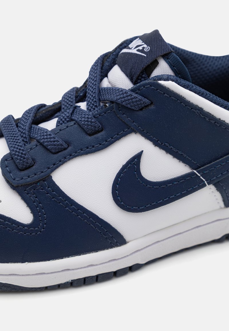 Baskets bleu marine et blanches en matériaux cuir et mesh. Présentent des lacets, un logo swoosh bien en vue, et une semelle en caoutchouc texturée.