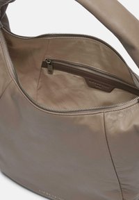 Skórzana torebka w jasnobrązowym kolorze o gładkiej fakturze, z kieszenią na zamek wewnątrz i detalem z logo, w kształcie zaokrąglonym.