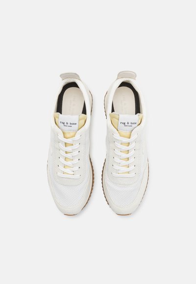 White mesh sneakers with cream-colored accents, textured rubber sole, and prominent laces. Features branding on the tongue.