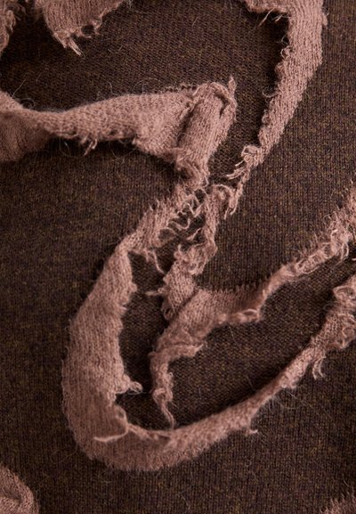 Strukturierter brauner Stoff mit ausgefransten Kanten in einer helleren Braunfarbe, der ein geschichtetes Design mit weichen Strängen und unregelmäßigen Formen schafft.
