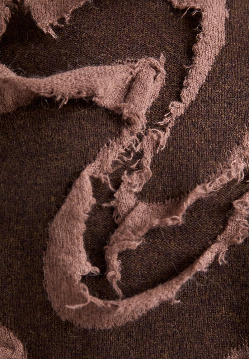 Gestructureerde bruine stof heeft rafelige randen in een lichtere bruine kleur, wat een gelaagd ontwerp creëert met zachte strengen en oneven vormen.