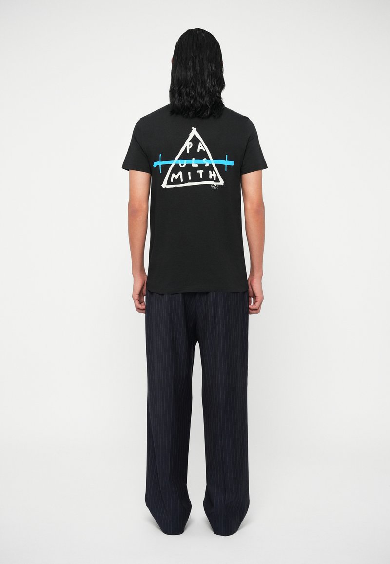 Melna kokvilnas T-krekla ar trīsstūru grafiku, kurā rakstīts "PAUL SMITH" baltā un zilā krāsā. Apvienots ar brīviem pinstrīpu biksēm.