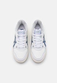 Bílé kožené tenisky s modrými akcenty. Perforovaný přední část, polstrovaný jazyk a šněrování. Logo ASICS na jazyku a na boku. Plochá gumová podrážka.