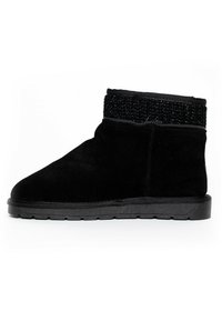 Bota negra de ante hasta el tobillo con un cuello de tela tejida texturizada, suela de goma plana y un diseño minimalista sin elementos decorativos visibles.