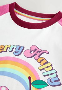 Valge puuvillane T-särk bordoopunase kraega ja roosade varrukatega, millel on värvikad vikerkaaregraafikud ning mänguliste fontidega tekst "Kirsi Õnnelik".