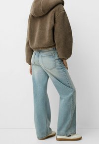 Bruine fleece hoodie met een cropped ontwerp gecombineerd met lichtblauwe jeans met wijde pijpen. Schoenen met een witte bovenkant en een gumzool.