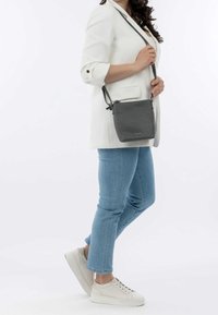 Borsa a tracolla grigia in pelle con finitura strutturata, forma rettangolare, tracolla regolabile e semplice hardware metallico, tenuta da una persona.