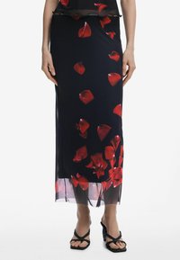 Schwarzer transparenter Rock mit rotem Blütenblattmuster, gerader Schnitt und seitlichem Schlitz. Getragen mit schwarzen Riemchensandalen, die eine fließende Textur zur Geltung bringen.
