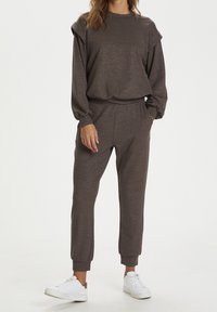 Brązowy sweter dzianinowy i dopasowane dresy z prążkowanymi mankietami. Posiada bufiaste rękawy i boczne kieszenie, w połączeniu z białymi sneakersami.