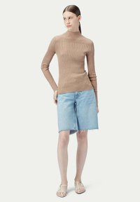 Beige ribbad stickad långärmad topp i kombination med ljusblå denimbermuda-shorts, designad med fransad nederkant och minimalistiska sandaler.