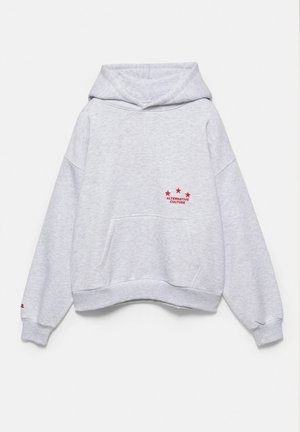 Sweat à capuche gris clair avec poche avant et texte rouge "Alternative Culture" sous trois étoiles rouges sur la partie gauche de la poitrine.