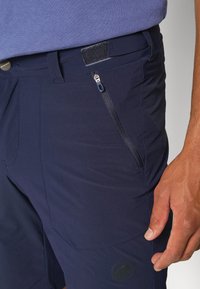 Navy outdoor šortky s hladkým materiálem, bočním zipovým kapsou, elastickým pasem a logem na dolní části nohavice.