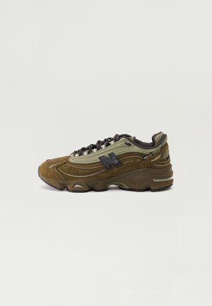 Brun og olivengrøn New Balance sneaker med sorte snørebånd, tyk sål og Cordura stoflabel på siden mod en ensartet lys baggrund.