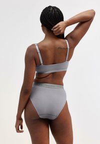 Šedý bavlněný bralet a vysoké kalhotky s elastickým pasem. Jednoduchý design s nastavitelnými ramínky a hladkou texturou, bez vzorů.