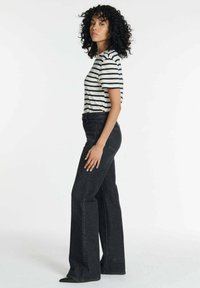 Zwarte hoge taille wide-leg jeans gecombineerd met een marineblauw en wit gestreept T-shirt met korte mouwen, gepresenteerd in een zijprofiel stand.