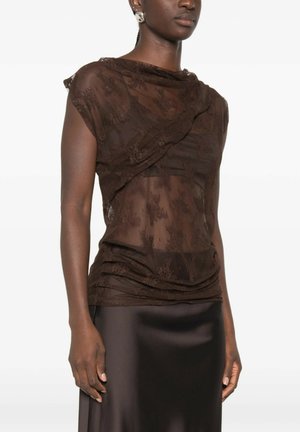 Donna che indossa un top in pizzo marrone scuro trasparente sopra un top abbinato e una gonna in raso scuro, con orecchini decorativi visibili.
