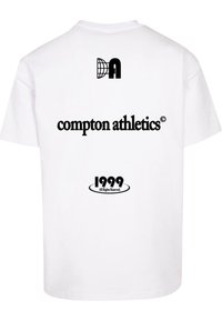White cotton t-shirt featuring black printed text: "DA" logo, "compton athletics," and "1999 All Rights Reserved" at the back.
