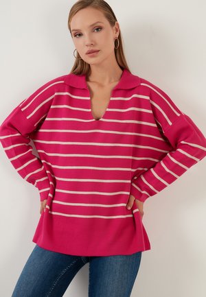 Long-sleeve pink knit sweater with white horizontal stripes, V-neck collar, and relaxed fit, paired with blue jeans.