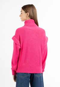 Maglione rosa a collo alto con lavorazione a maglia testurizzata, maniche oversize e polsini a costine. Abbinato a jeans in denim a vita alta. Vista dal retro.