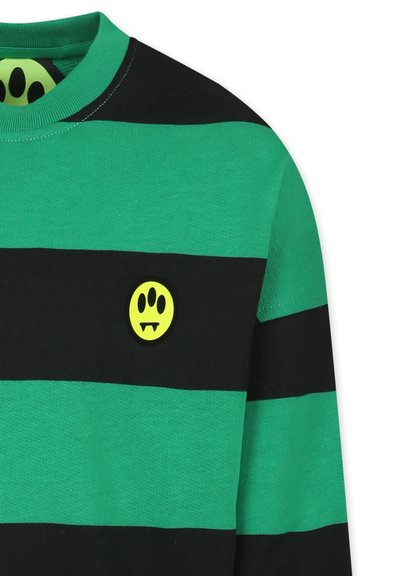 Maglione a righe verdi e nere con una grafica rotonda gialla che presenta un volto con zanne, e colletto a girocollo. Tessuto morbido.
