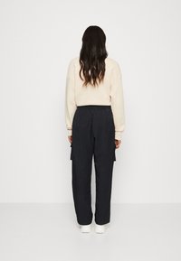 Mikina světle béžové barvy nošena s černými cargo kalhotami; kalhoty mají dvě boční kapsy, elastický pas a mírně strukturovanou tkaninu.