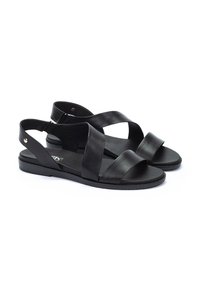 Sandalias de cuero negro con correas entrecruzadas, diseño de punta abierta, suela plana y acentos de hardware minimalistas. Textura suave, estilo casual.