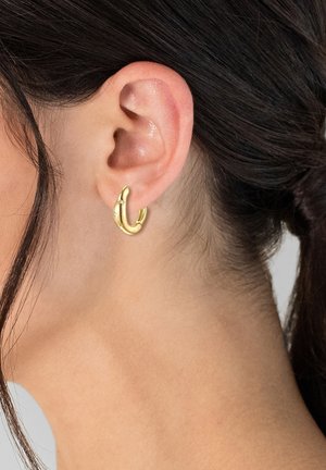 Goldene Creolen mit einem gewickelten Design, das eine glatte Oberfläche und einen leichten Glanz aufweist. Sie werden am Ohrläppchen getragen, wodurch ihre kreisrunde Form betont wird.